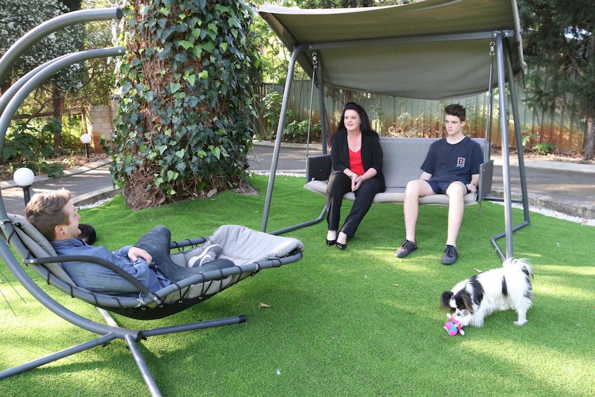 Family members sit on a swing in the backyard.