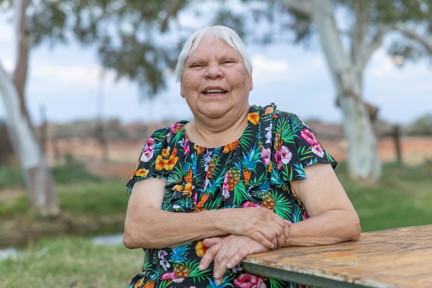 A First Nations woman stands on her country in remote Australia and smiles. 