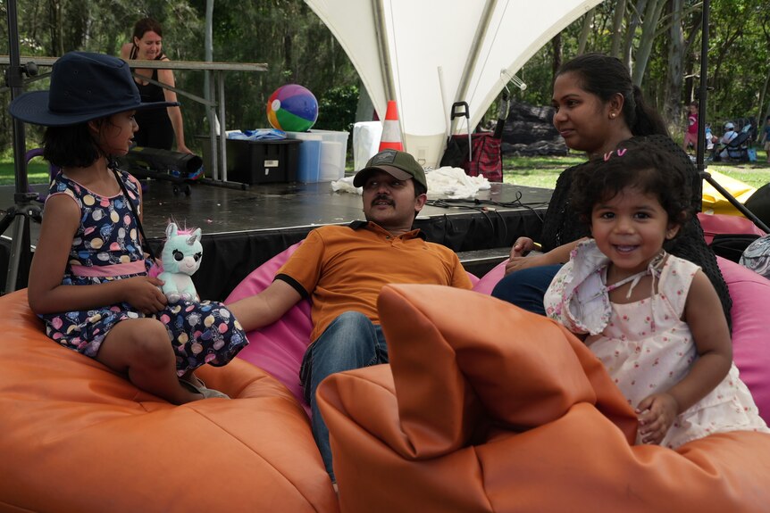 a man, woman and two small children sit back on bean bags in a park, in the shade