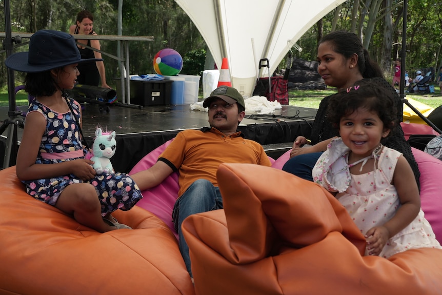 a man, woman and two small children sit back on bean bags in a park, in the shade