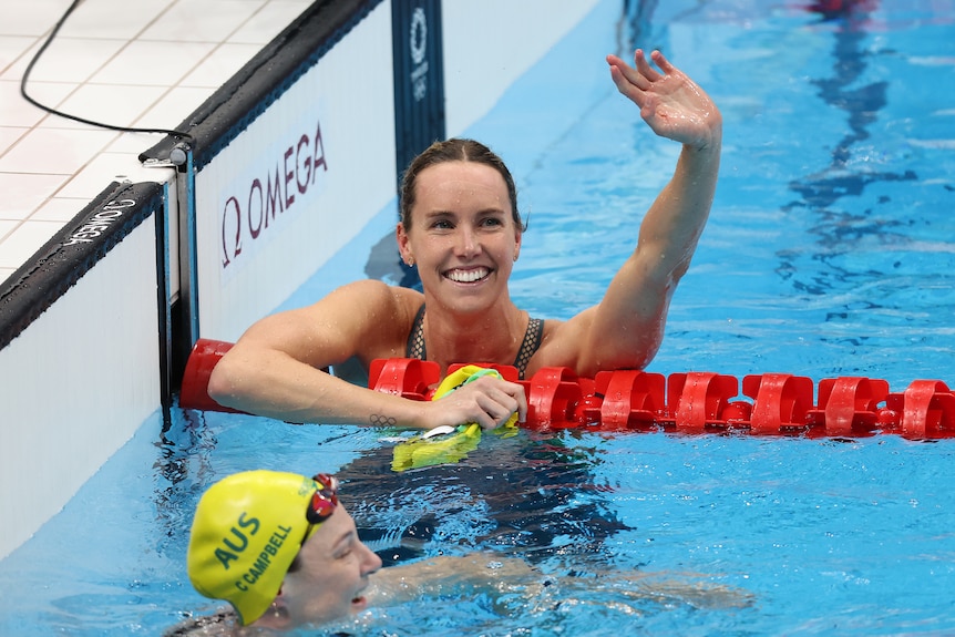 A woman wearing green swimmers in a pool holds her arm up in the air