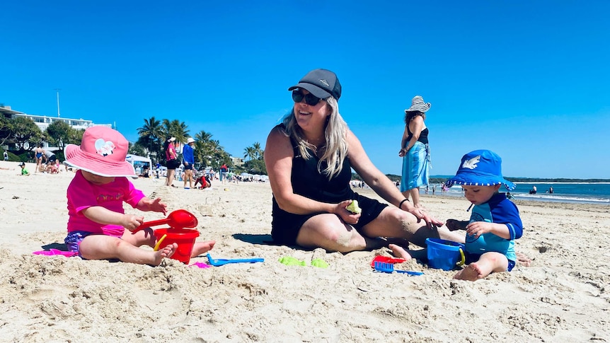 Mum Natalie Fullager sits on the beach with her twins