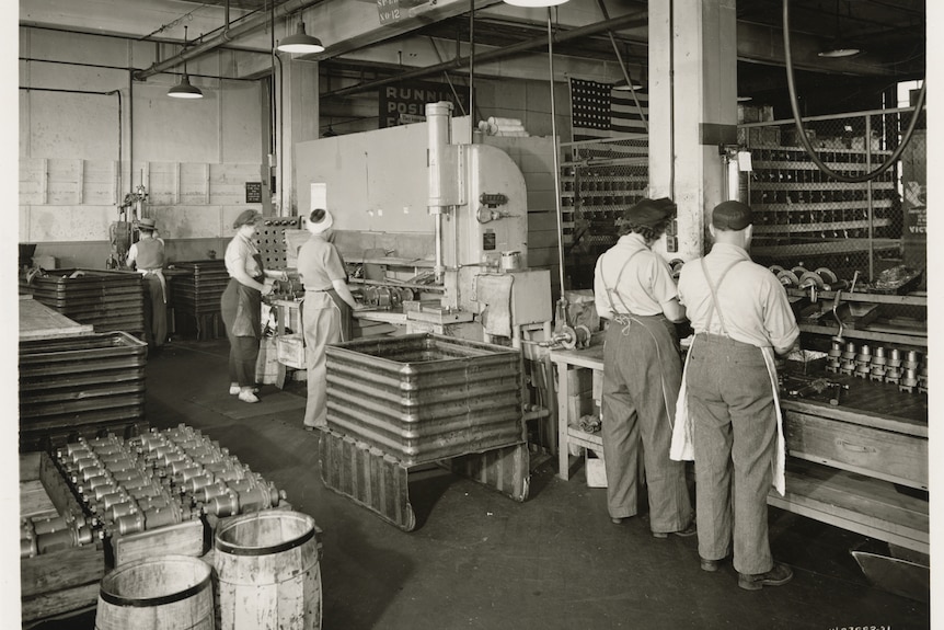 Monochrome of men and women on wartime production line.