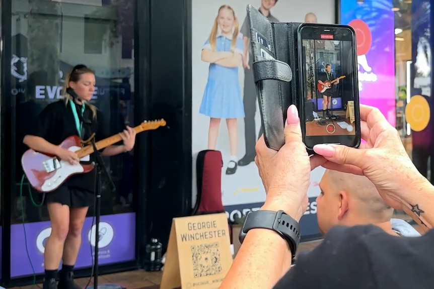 A woman playing the guitar is filmed on a phone