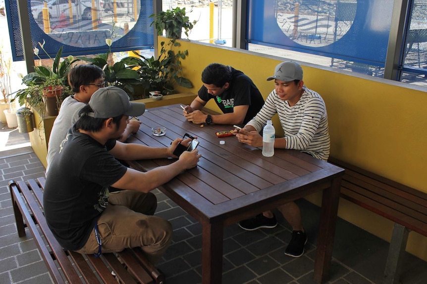 A group pf young Filipino men sit at a table texting.