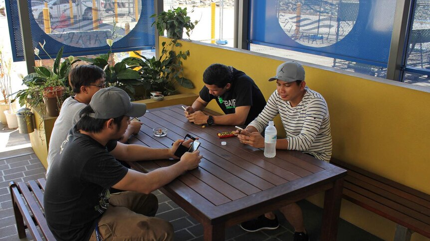 A group pf young Filipino men sit at a table texting.