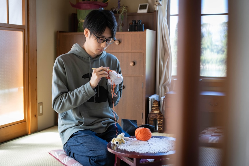 A young man crochets.