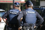 Police officers, facing away from the camera, standing around in a city.