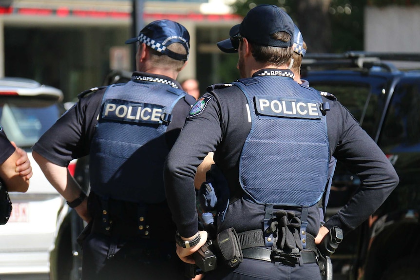 Police officers, facing away from the camera, standing around in a city.