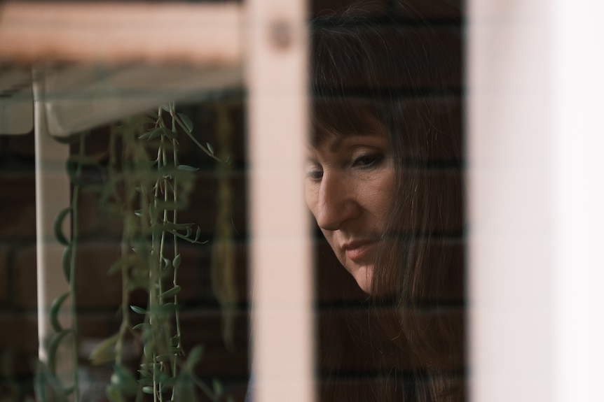 A close up of Kim's face through the glass of a greenhouse.