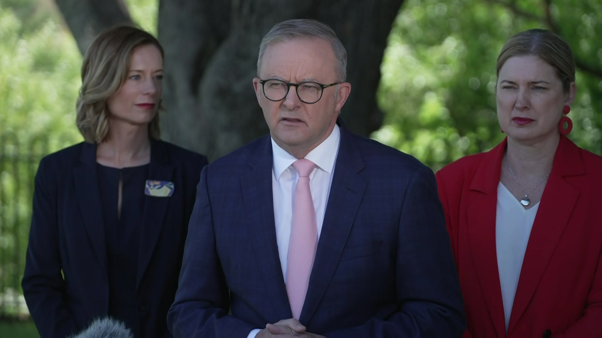 Prime Minister wears glasses and suit standing outside for press conference. 