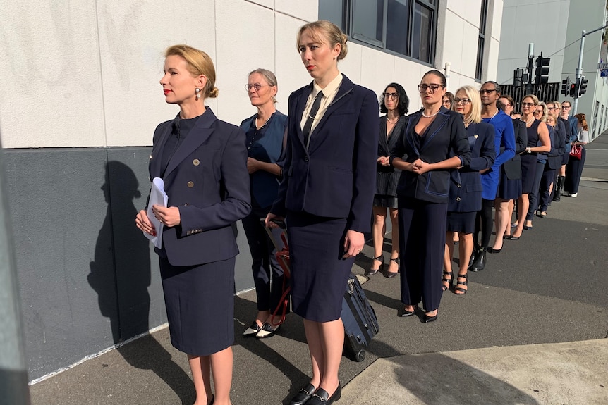 Kirsha Kaechele stands in front of a line of women, all wearing navy blue, on a footpath in Hobart