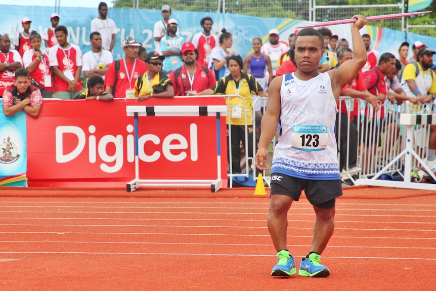 Iosefo stands at the start of his javelin run-up inside an athletics stadium. A crowd behind watches on.