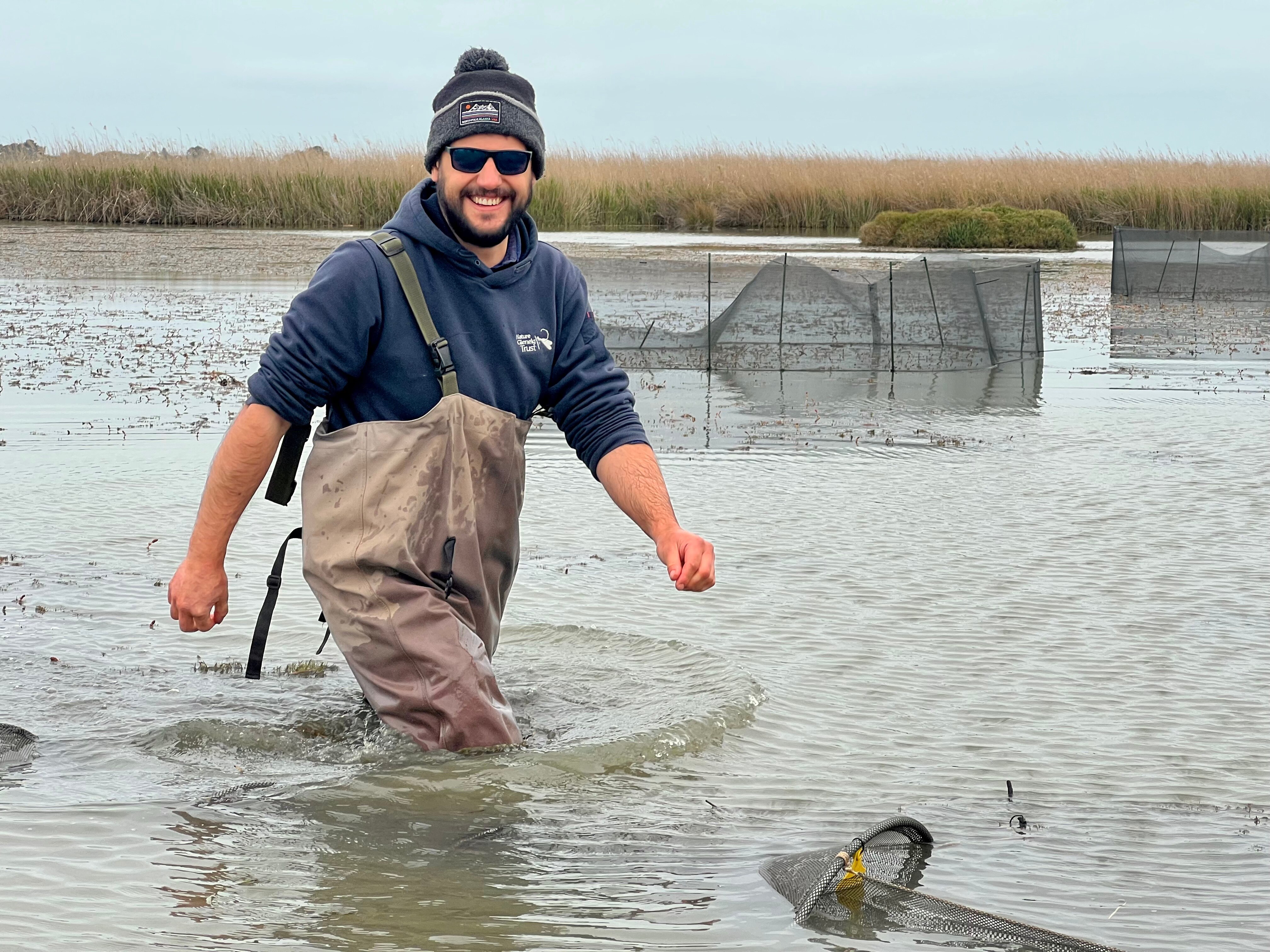 A man in waders walks through the water of a river.