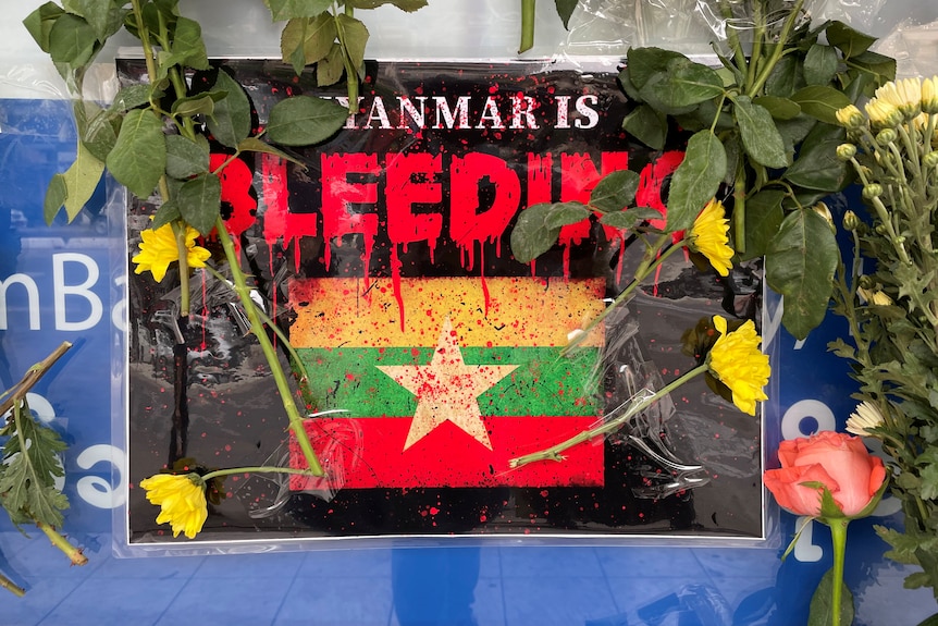 A placard reads 'Myanmar is bleeding' alongside flowers