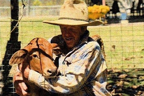 Man in akubra hat cuddling a calf