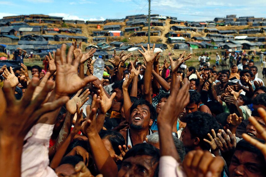 What looks like hundreds of men stretch out their arms as aid arrives in Bangladesh