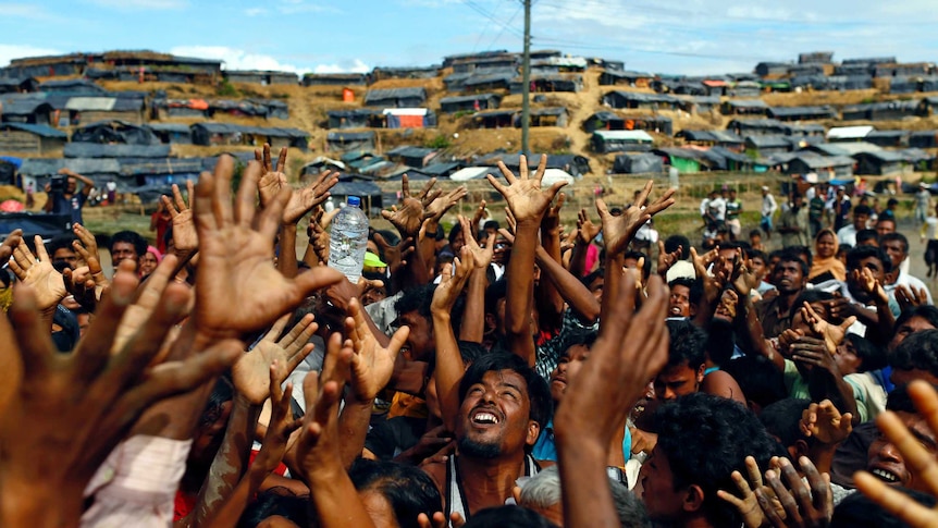 What looks like hundreds of men stretch out their arms as aid arrives in Bangladesh