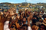 What looks like hundreds of men stretch out their arms as aid arrives in Bangladesh