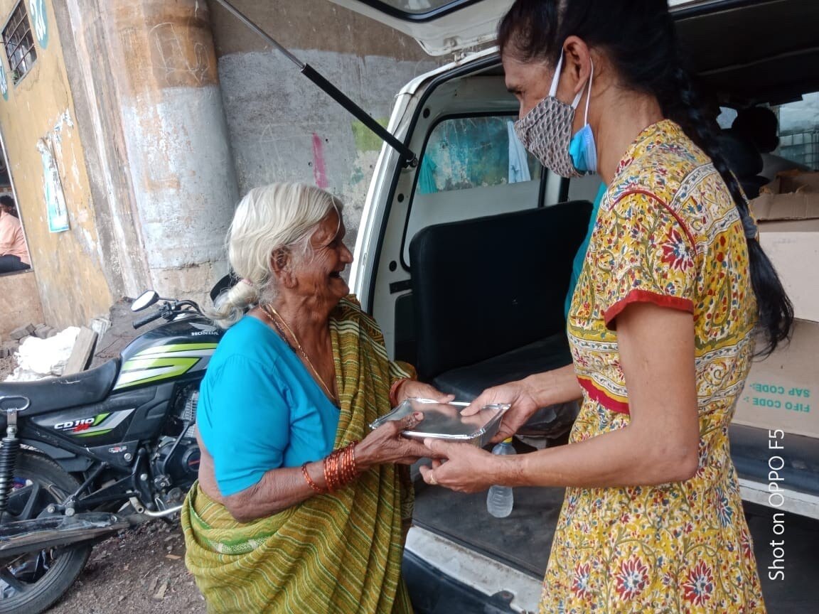 A woman handing an elderly woman food in India. 
