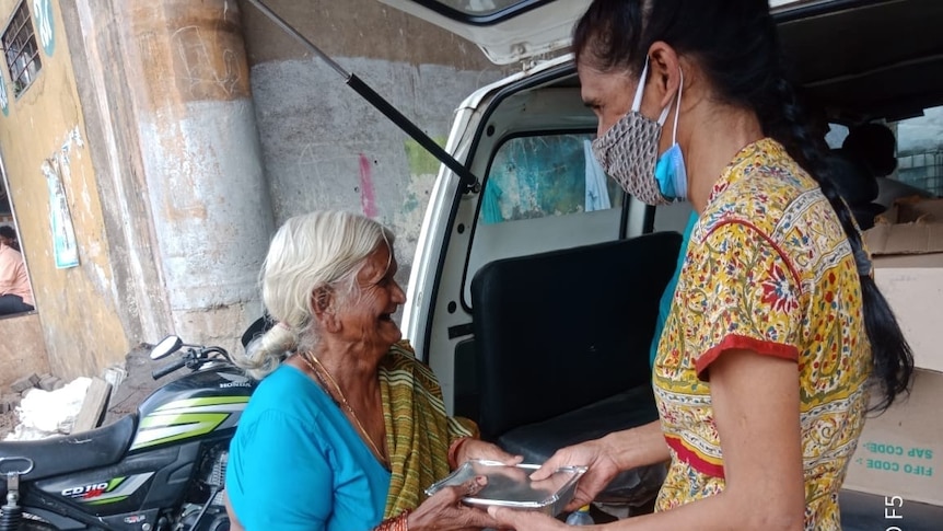 A woman handing an elderly woman food in India. 