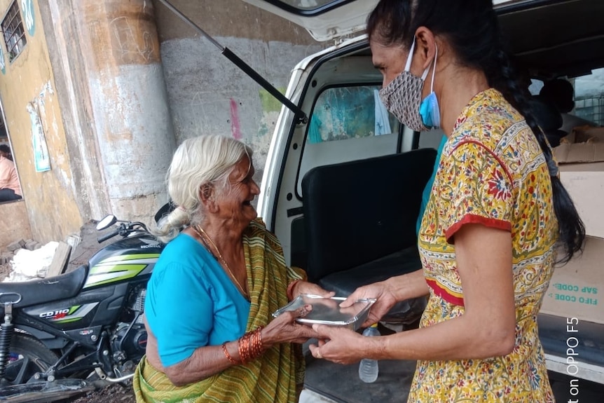 A woman handing an elderly woman food in India. 