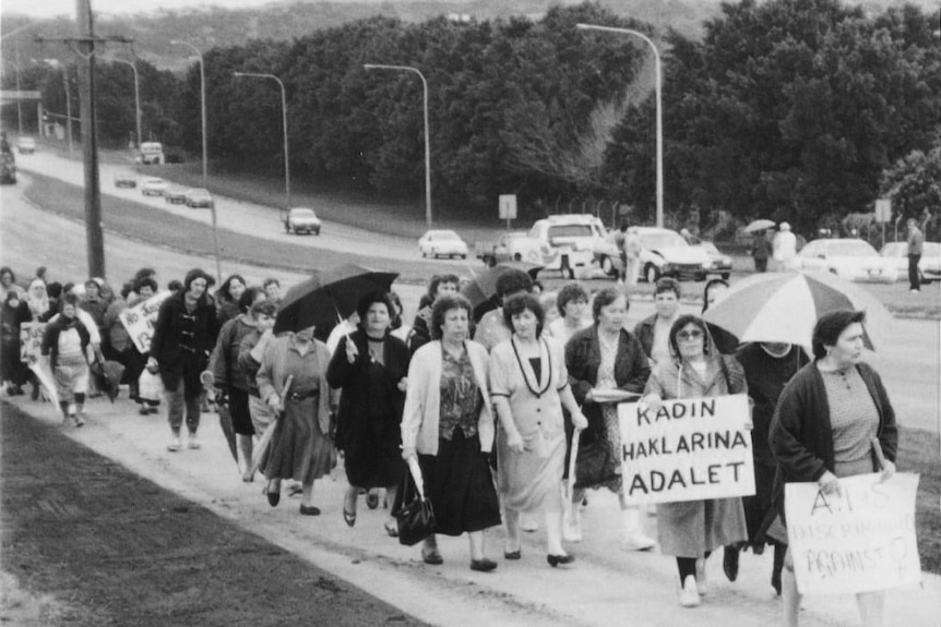 Women march along a footpath holding signs and umbrellas.