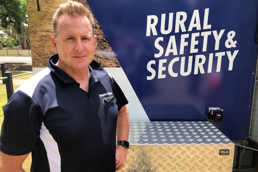 a man stands in a Victoria Police polo shirt with the message 'rural safety and security' behind him