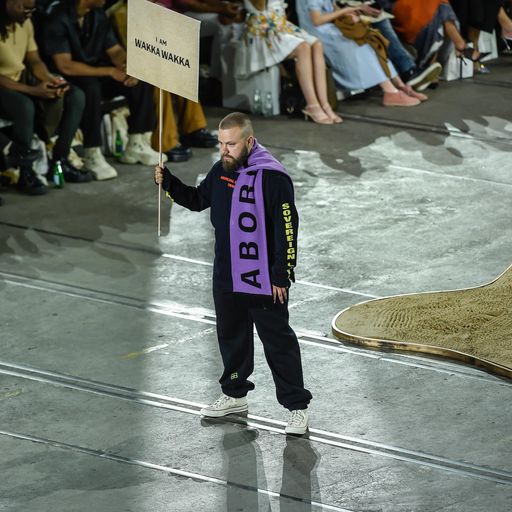 A man holding a sign. He has a scarf draped across his shoulder.