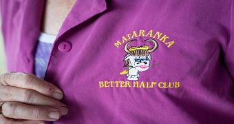 A purple shirt with an embroidered logo of a cartoon cow wearing lipstick and makeup with a yellow rose in its mouth.