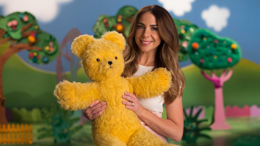 A woman holds a big yellow teddy bear