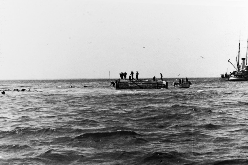 A black and white photo shows divers on an ocean pontoon leaping off it.