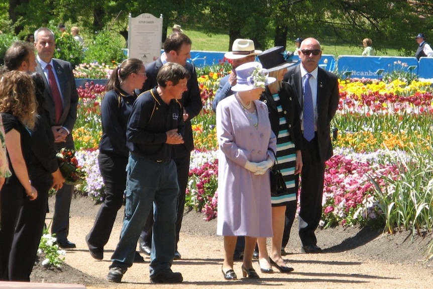 Some gardeners walk amongst tulip beds on a sunny day with the Queen.