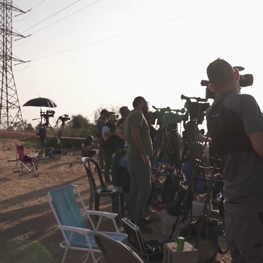 You view a video screenshot showing a range of journalists and cameras in a desert landscape. 