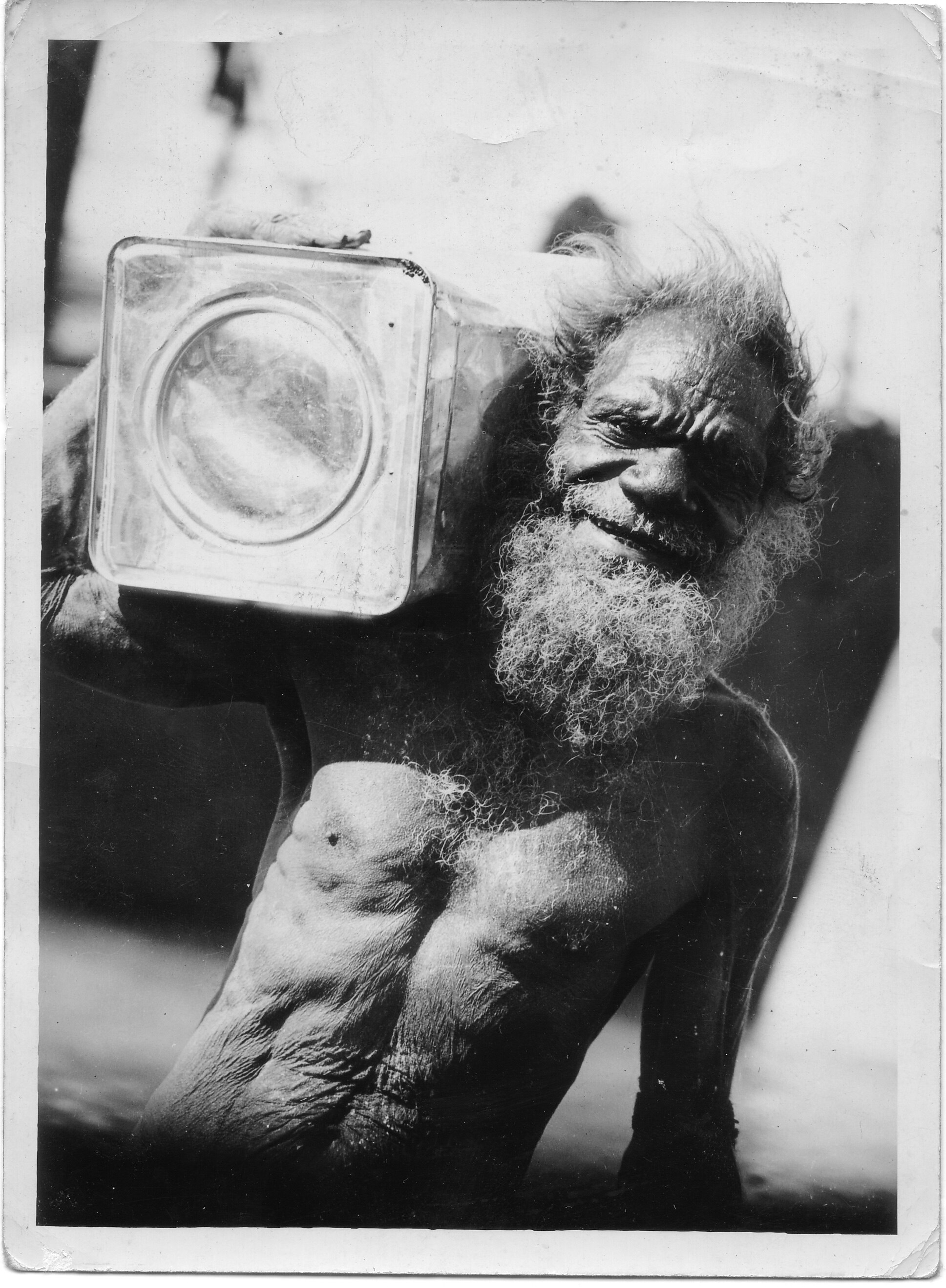 Bearded man carrying tin on shoulder, smiling. bare-chested. monochrome.