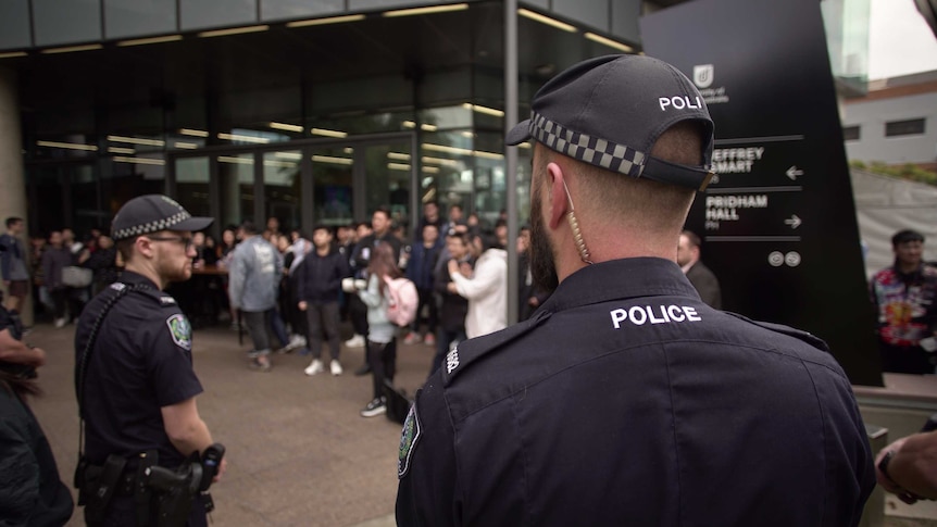 Two police officers stand among hundreds of protesters in front of a university building