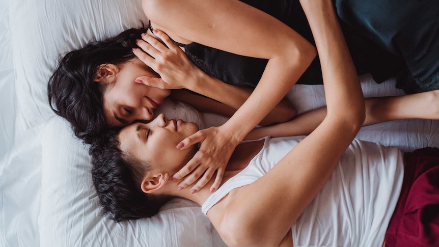 Two women lay in bed looking at one another in a story about ways to improve your sex life today.