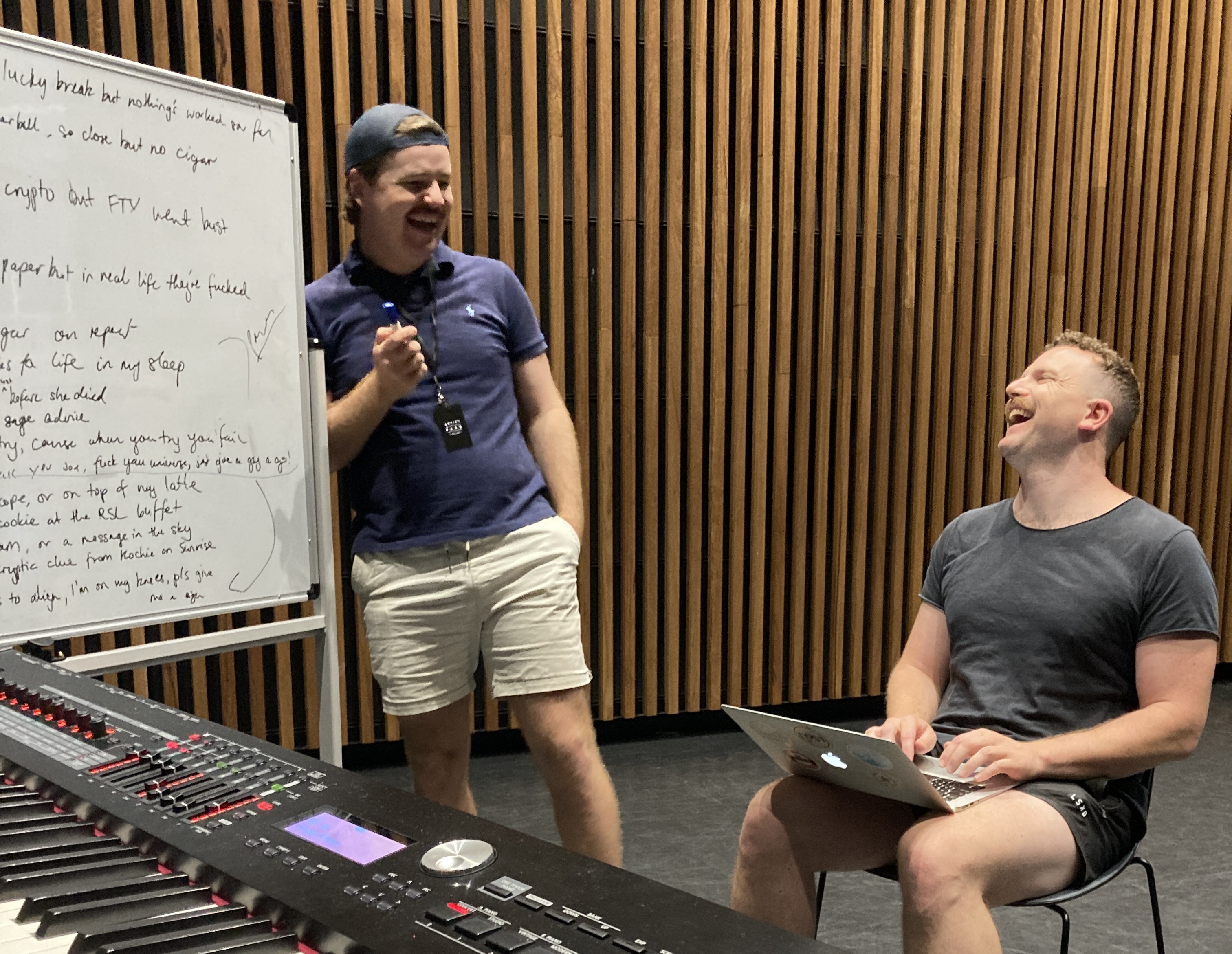 man stands next to a white board, looking at man who is sitting down with a laptop.