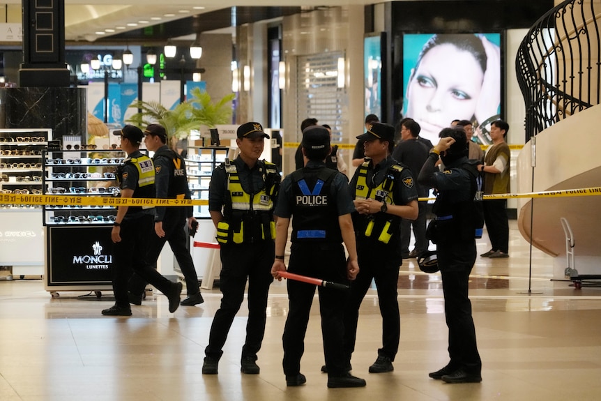 Uniformed police officers cordon off a crime scene near shops inside a mall at a large subway station.