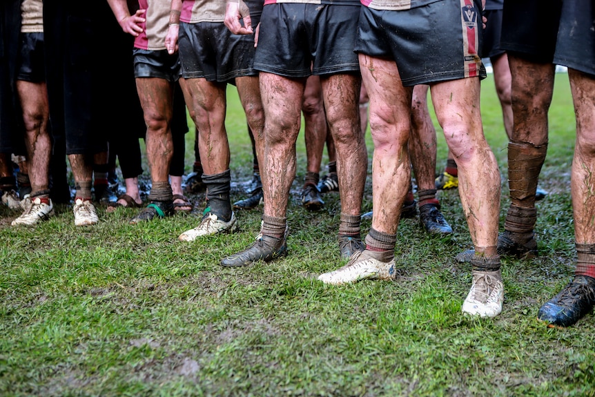 Row of football players legs streaked with mud