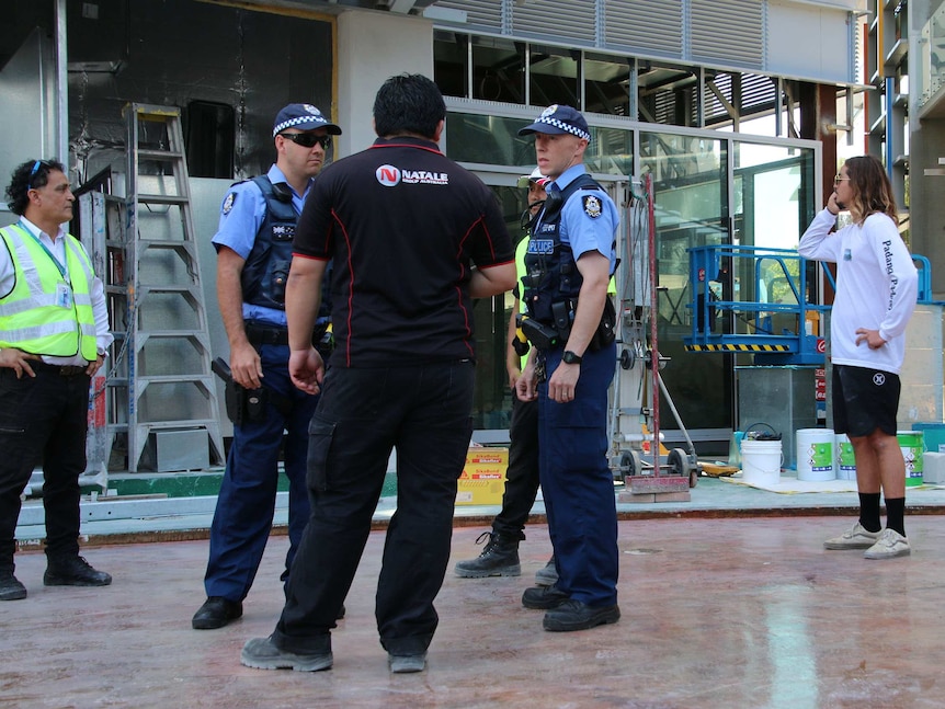 Police speak with security officers on the construction site, while another man speaks on the phone behind them.