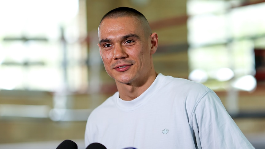 Australian boxer Tim Tszyu smiles at the media as he stands in front of a row of microphones.