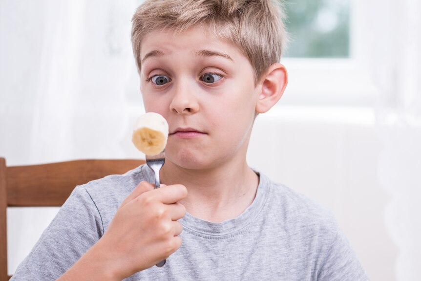 A boy looks at a piece of banana on a fork