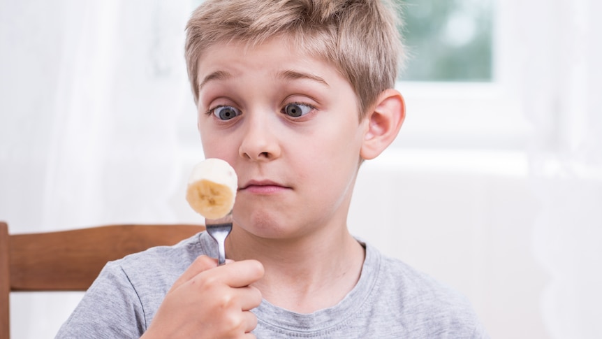 A boy looks at a piece of banana on a fork