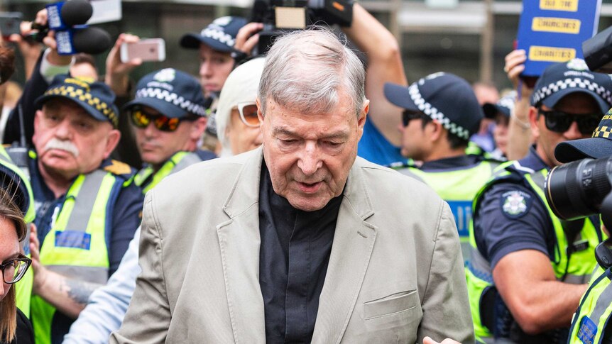Cardinal George Pell, wearing a brown suit, is surrounded by police as he walks to court.
