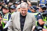 Cardinal George Pell, wearing a brown suit, is surrounded by police as he walks to court.