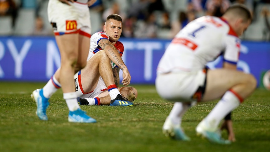 A male NRL player sits on the ground disappointed after his team lost.
