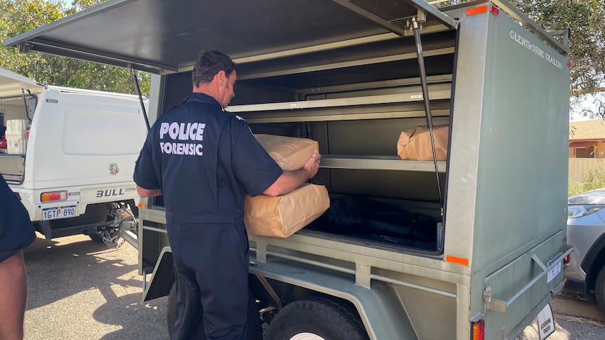 A police officer loads large paper bags into a trailer.
