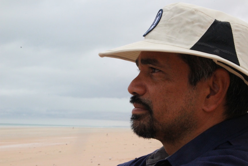 a man in a sun hat gazes out across a beach