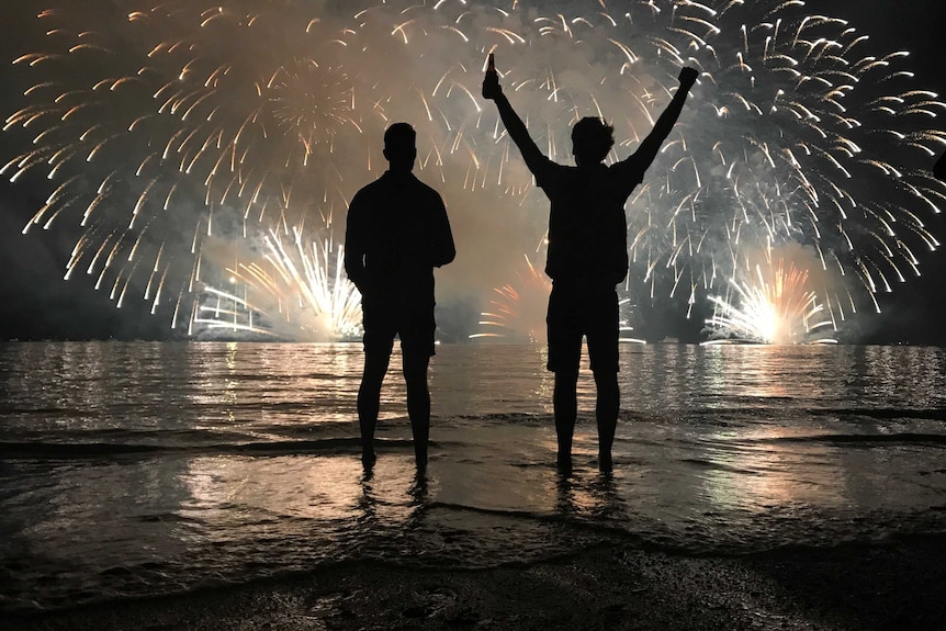 Two men in silhouette watch fireworks explode over Darwin